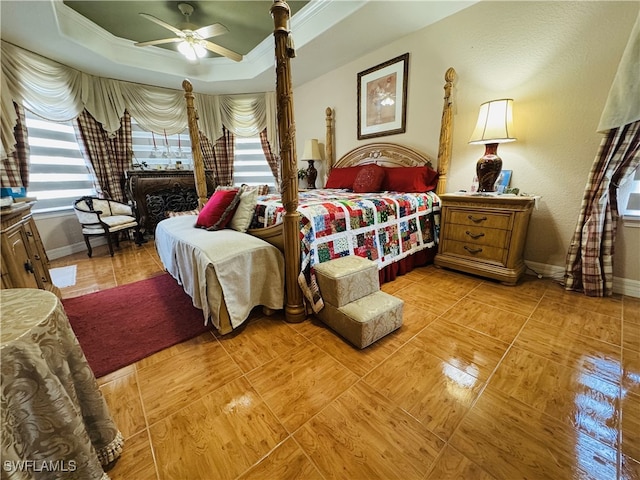 bedroom featuring a tray ceiling, multiple windows, ceiling fan, and baseboards