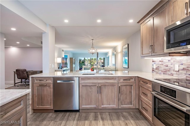 kitchen featuring pendant lighting, decorative backsplash, light hardwood / wood-style floors, kitchen peninsula, and stainless steel appliances