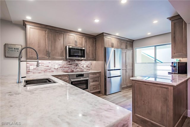 kitchen with sink, stainless steel appliances, light stone counters, light hardwood / wood-style floors, and decorative backsplash