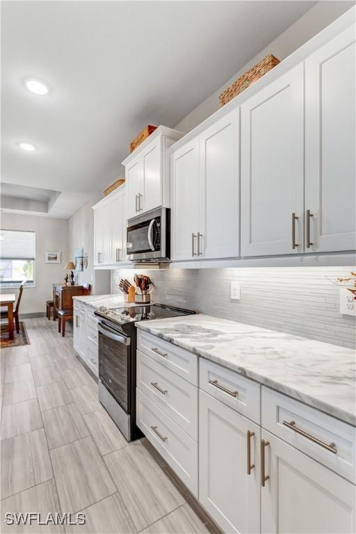 kitchen featuring stainless steel appliances, white cabinetry, tasteful backsplash, and light stone counters