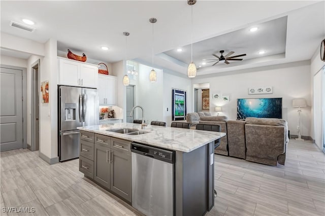 kitchen with white cabinetry, sink, stainless steel appliances, an island with sink, and a tray ceiling