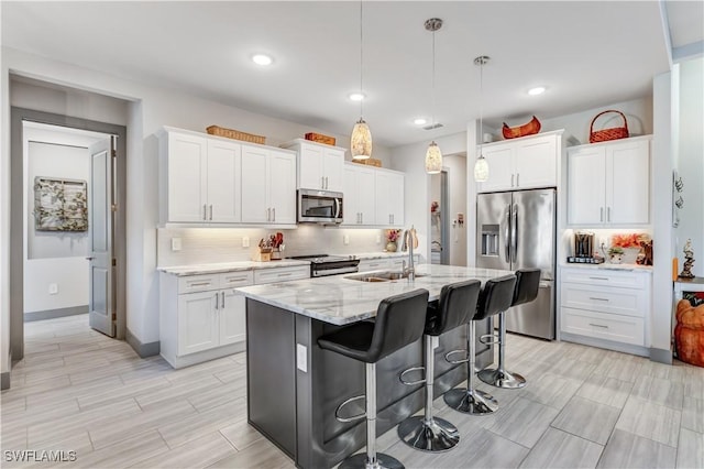 kitchen with stainless steel appliances, sink, decorative light fixtures, white cabinetry, and an island with sink