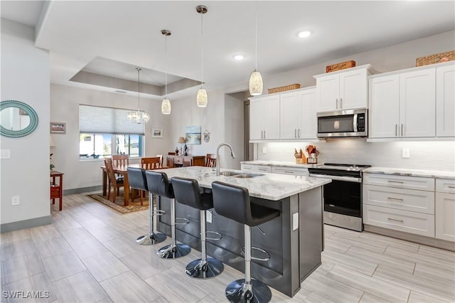 kitchen featuring a kitchen island with sink, sink, appliances with stainless steel finishes, decorative light fixtures, and white cabinetry