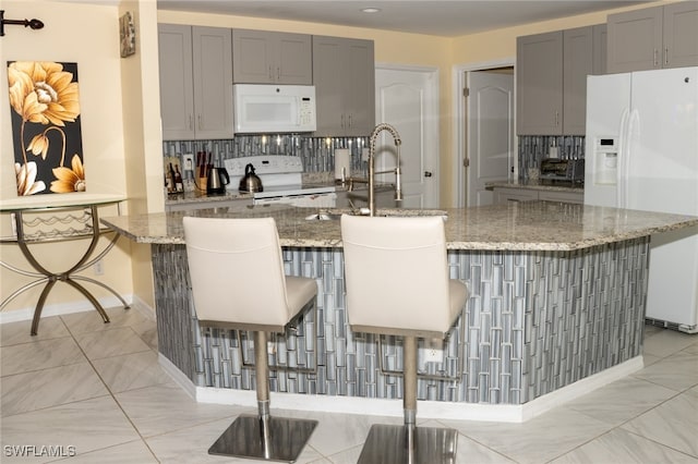 kitchen featuring a kitchen bar, light stone countertops, an island with sink, and white appliances