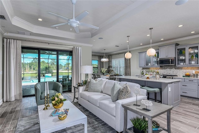 living room with hardwood / wood-style flooring, ceiling fan, crown molding, and a tray ceiling