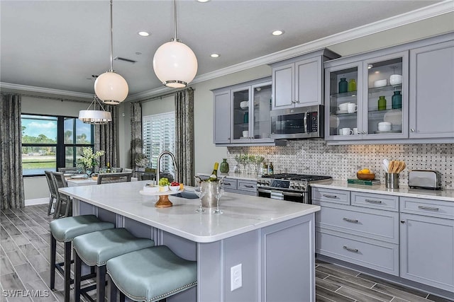 kitchen with gray cabinetry, hanging light fixtures, an island with sink, and stainless steel appliances