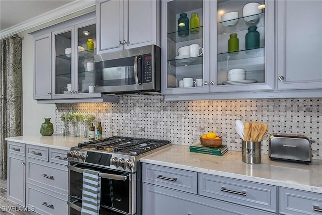 kitchen featuring appliances with stainless steel finishes, backsplash, light stone counters, gray cabinetry, and crown molding