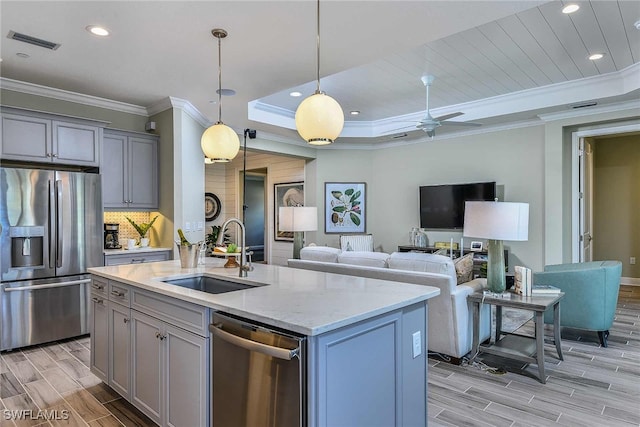 kitchen featuring sink, a raised ceiling, decorative light fixtures, a center island with sink, and appliances with stainless steel finishes