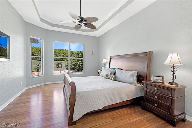 bedroom featuring ceiling fan, light wood-type flooring, and a tray ceiling