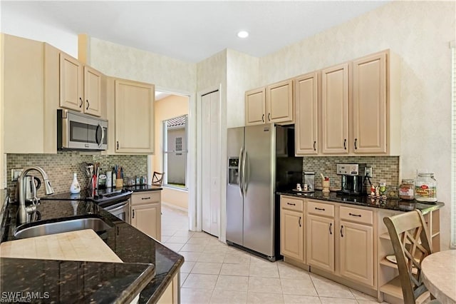 kitchen featuring sink, backsplash, dark stone counters, light tile patterned floors, and appliances with stainless steel finishes