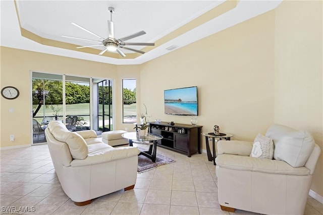 tiled living room with a raised ceiling, ceiling fan, and ornamental molding