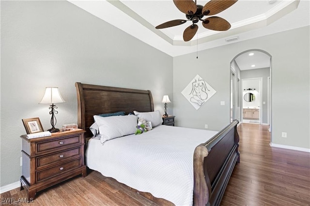 bedroom featuring ensuite bath, ceiling fan, dark wood-type flooring, a tray ceiling, and ornamental molding