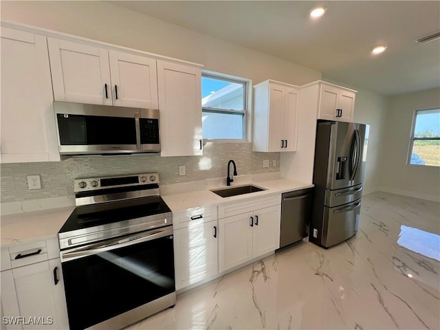 kitchen featuring appliances with stainless steel finishes, backsplash, a healthy amount of sunlight, sink, and white cabinetry