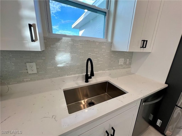 kitchen featuring dishwasher, sink, tasteful backsplash, light stone counters, and white cabinets