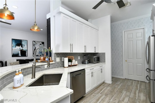 kitchen featuring sink, crown molding, appliances with stainless steel finishes, hanging light fixtures, and light stone countertops