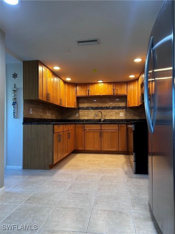 kitchen with dark stone countertops, black fridge, sink, and light tile patterned floors