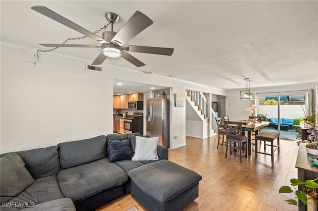 living area featuring visible vents, light wood-style flooring, stairway, crown molding, and ceiling fan