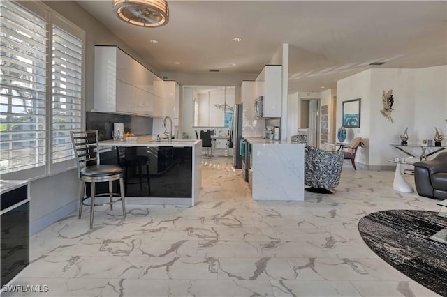 kitchen with a breakfast bar, sink, kitchen peninsula, appliances with stainless steel finishes, and white cabinetry