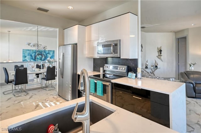 kitchen featuring sink, hanging light fixtures, decorative backsplash, white cabinetry, and stainless steel appliances