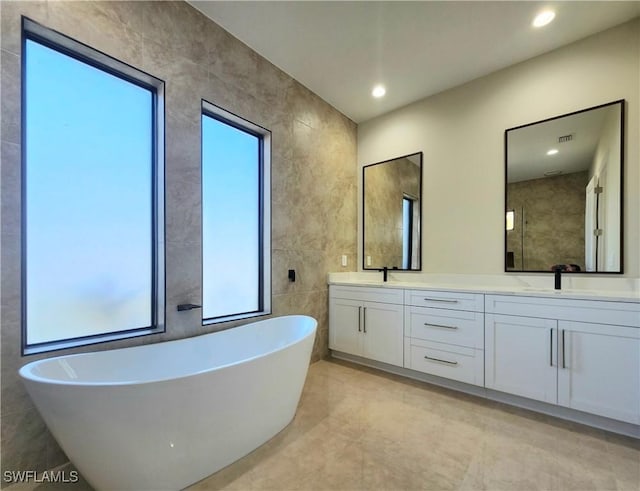 bathroom featuring vanity, a bath, and tile walls