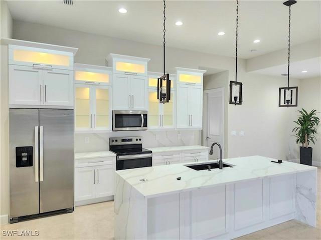 kitchen with light stone countertops, white cabinetry, sink, stainless steel appliances, and an island with sink