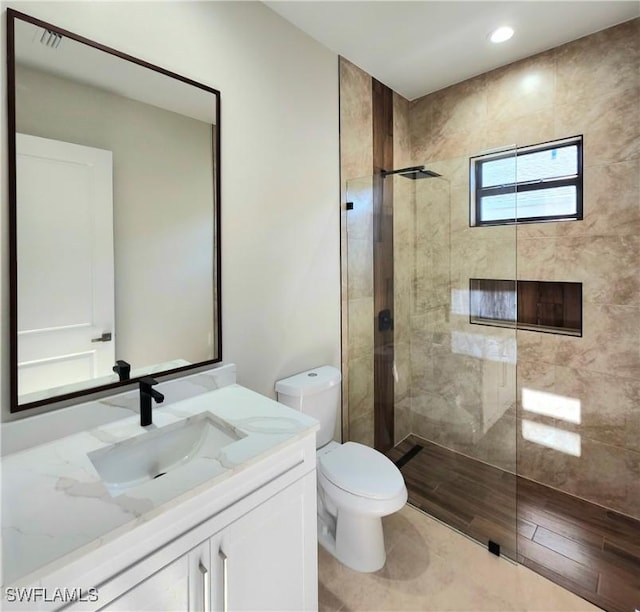 bathroom featuring a tile shower, vanity, and toilet