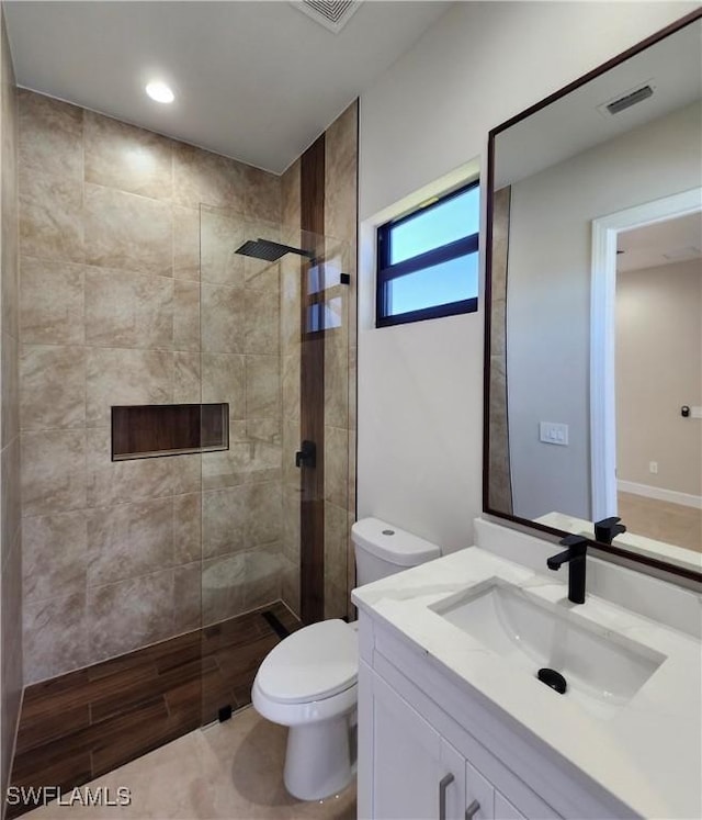 bathroom with a tile shower, vanity, and toilet