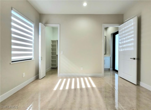 unfurnished bedroom featuring ensuite bathroom, a walk in closet, multiple windows, and a closet