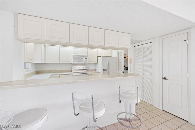 kitchen featuring a breakfast bar, light countertops, a peninsula, white appliances, and white cabinetry