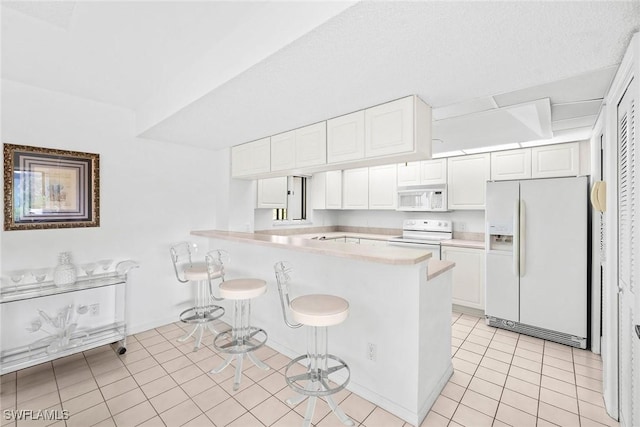 kitchen featuring a breakfast bar, white appliances, a peninsula, light countertops, and light tile patterned floors