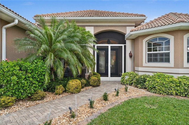 view of exterior entry with a tiled roof, stucco siding, and french doors