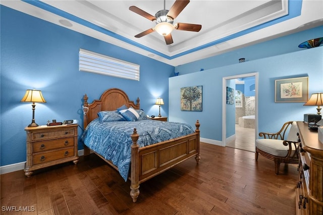 bedroom featuring dark wood-style floors, a tray ceiling, ensuite bath, and baseboards