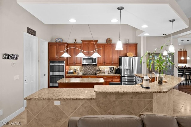 kitchen featuring light tile patterned floors, tasteful backsplash, brown cabinets, stainless steel appliances, and a large island with sink