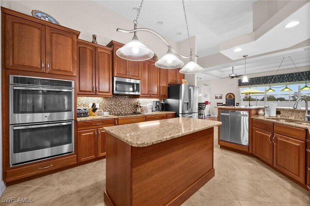 kitchen with stainless steel appliances, backsplash, a sink, a kitchen island, and light stone countertops