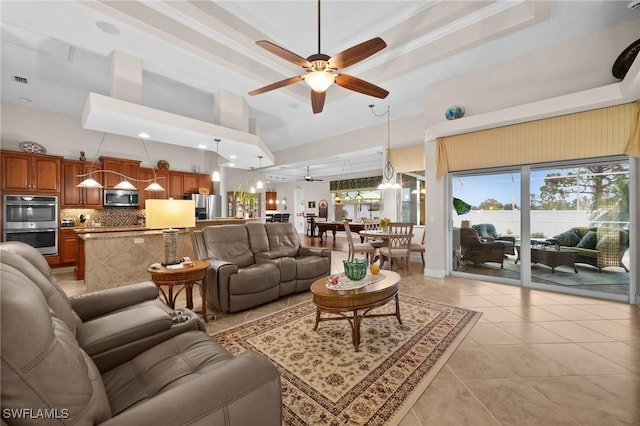 living room featuring ceiling fan, a high ceiling, a tray ceiling, crown molding, and light tile patterned flooring