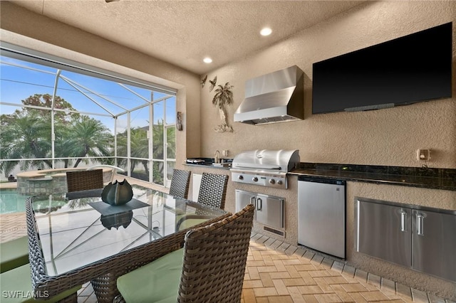 kitchen featuring fridge, wall chimney exhaust hood, brick floor, and a textured wall