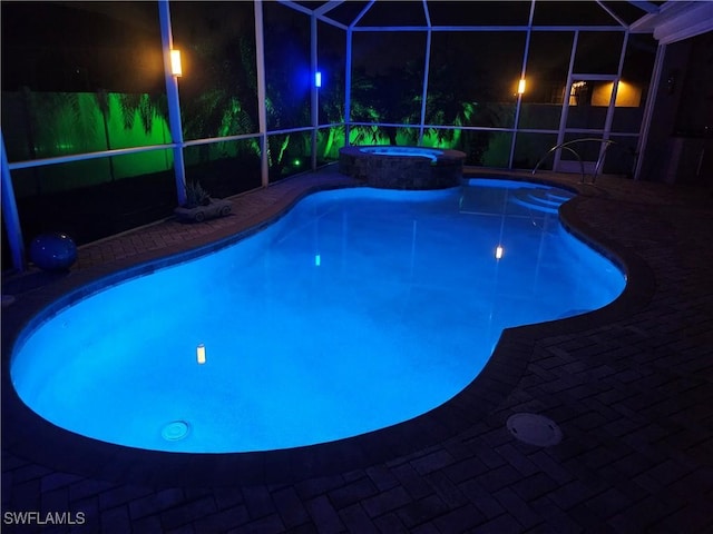 pool at night featuring a lanai, a patio area, and a pool with connected hot tub