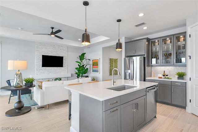 kitchen with gray cabinetry, a kitchen island with sink, sink, and appliances with stainless steel finishes