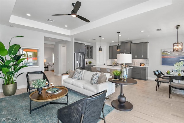 living room with light wood-type flooring, a raised ceiling, and ceiling fan