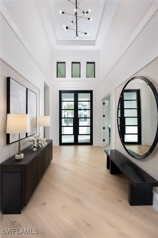 foyer entrance with french doors, a towering ceiling, light hardwood / wood-style floors, and a notable chandelier