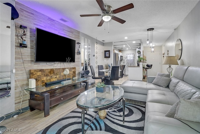 living room featuring ceiling fan, light hardwood / wood-style floors, and a textured ceiling