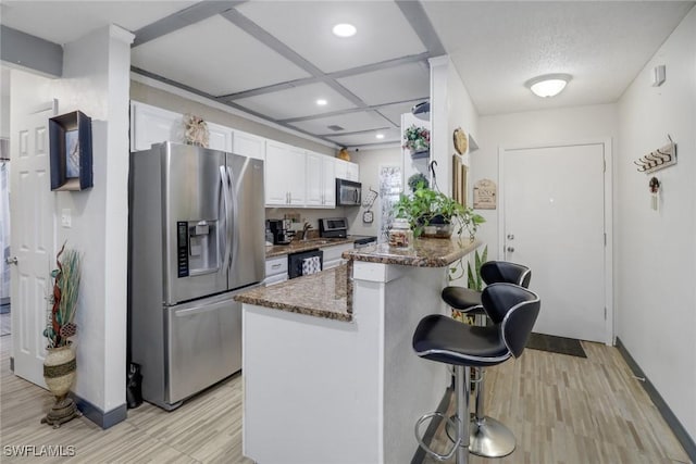 kitchen featuring dark stone countertops, kitchen peninsula, a breakfast bar area, white cabinets, and appliances with stainless steel finishes