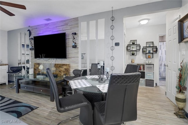 dining space featuring light wood-style flooring, an accent wall, visible vents, and a ceiling fan