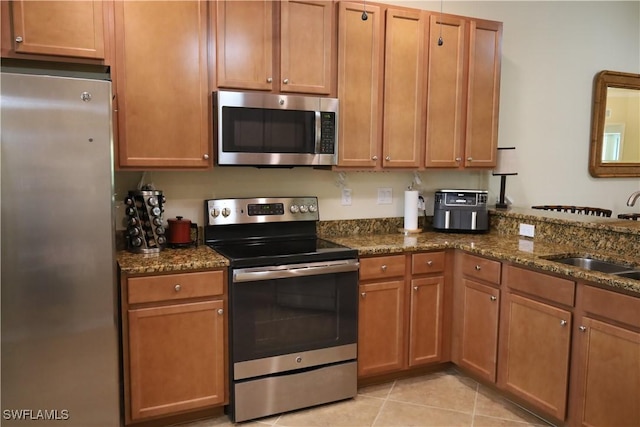 kitchen featuring light tile patterned floors, dark stone countertops, a sink, and stainless steel appliances