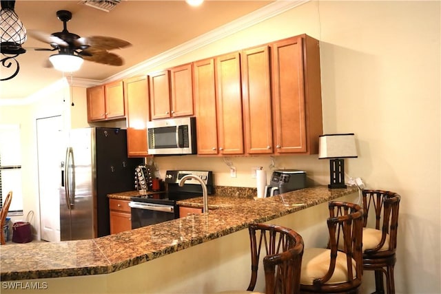 kitchen featuring crown molding, a breakfast bar, visible vents, stainless steel appliances, and a ceiling fan