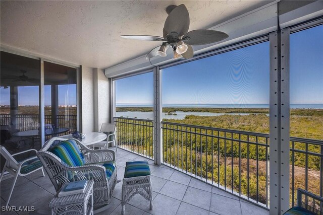 sunroom with ceiling fan and a water view