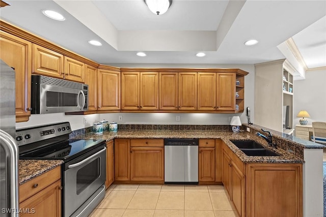 kitchen with kitchen peninsula, appliances with stainless steel finishes, ornamental molding, sink, and dark stone countertops