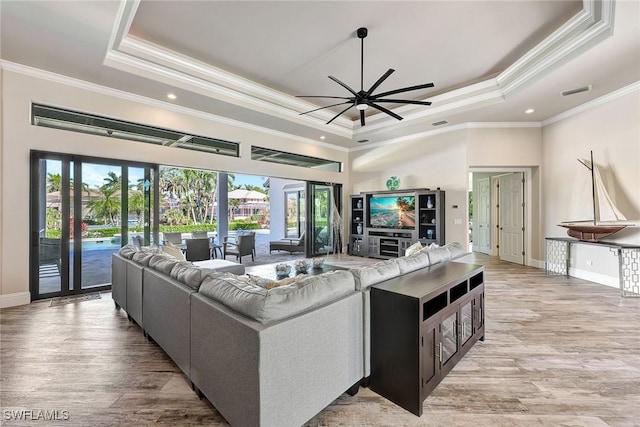 living room with a raised ceiling, ceiling fan, and ornamental molding