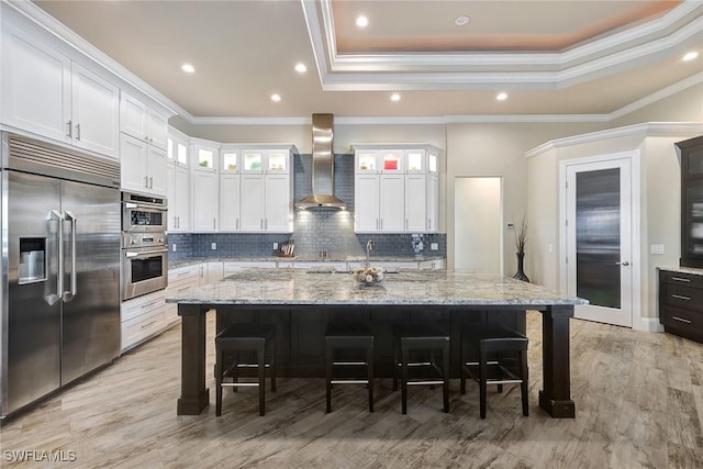 kitchen with appliances with stainless steel finishes, white cabinetry, a large island, and wall chimney range hood