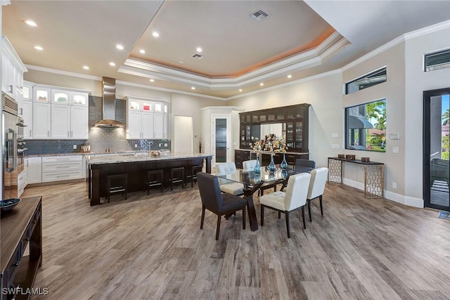 dining space featuring light wood-type flooring, a raised ceiling, and crown molding